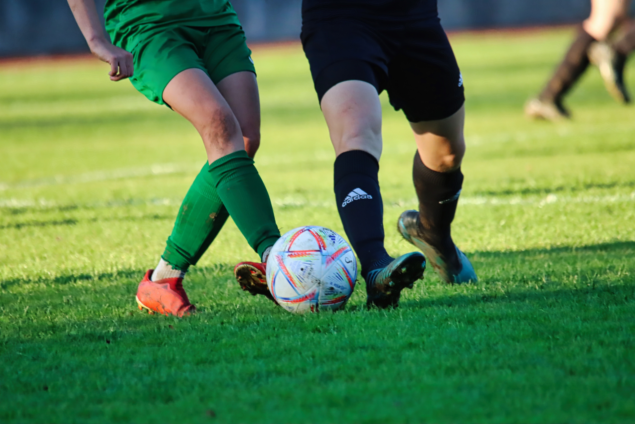 Two soccer players kicking the ball on a green field.