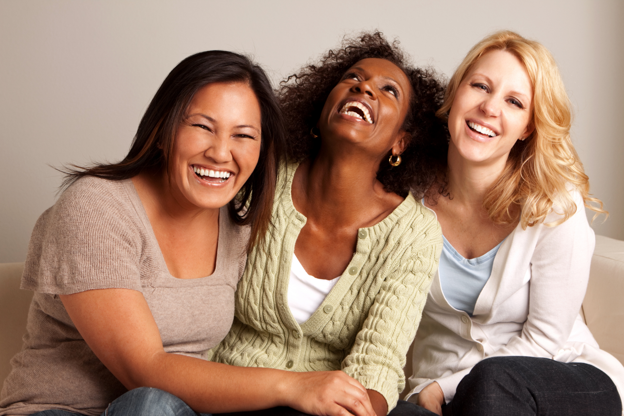 Three women are laughing while sitting on a couch.