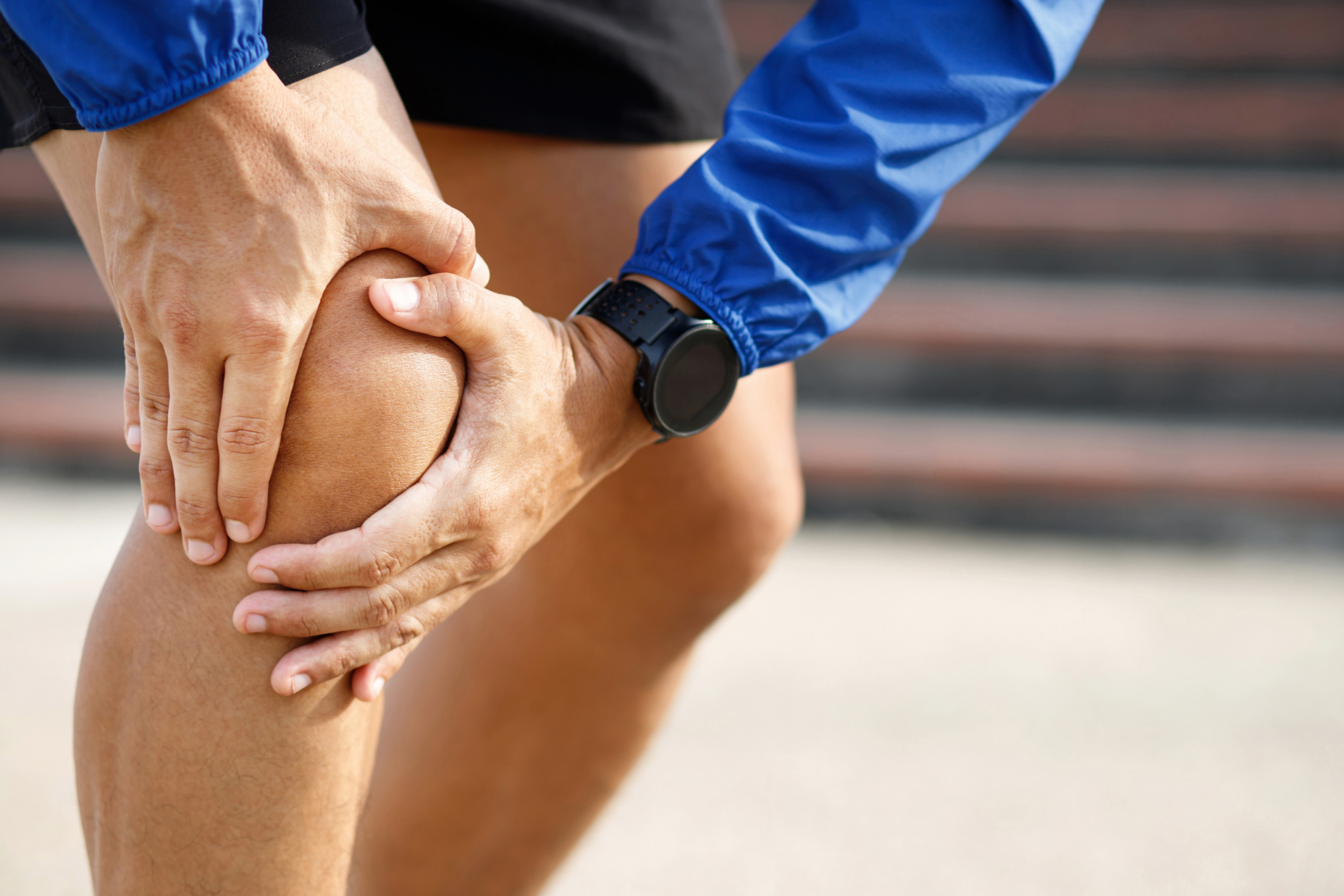 An individual with joint pain is holding his knee.
