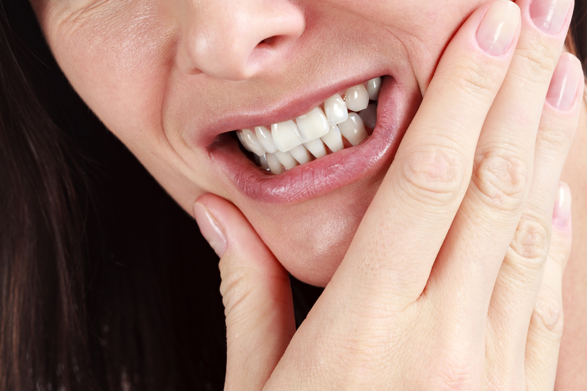 A woman with a facial & jaw pain is holding her hand.